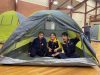Three happy children in scout uniforms inside a dome tent