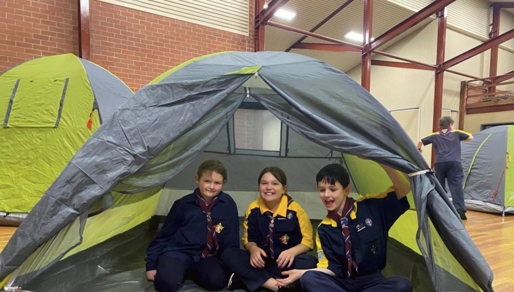 Three happy children in scout uniforms inside a dome tent