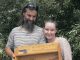 A man with dark long hair and beard and smiling woman holding a wooden display rack with tins of hemp products Pain Balm and Save Your Skin